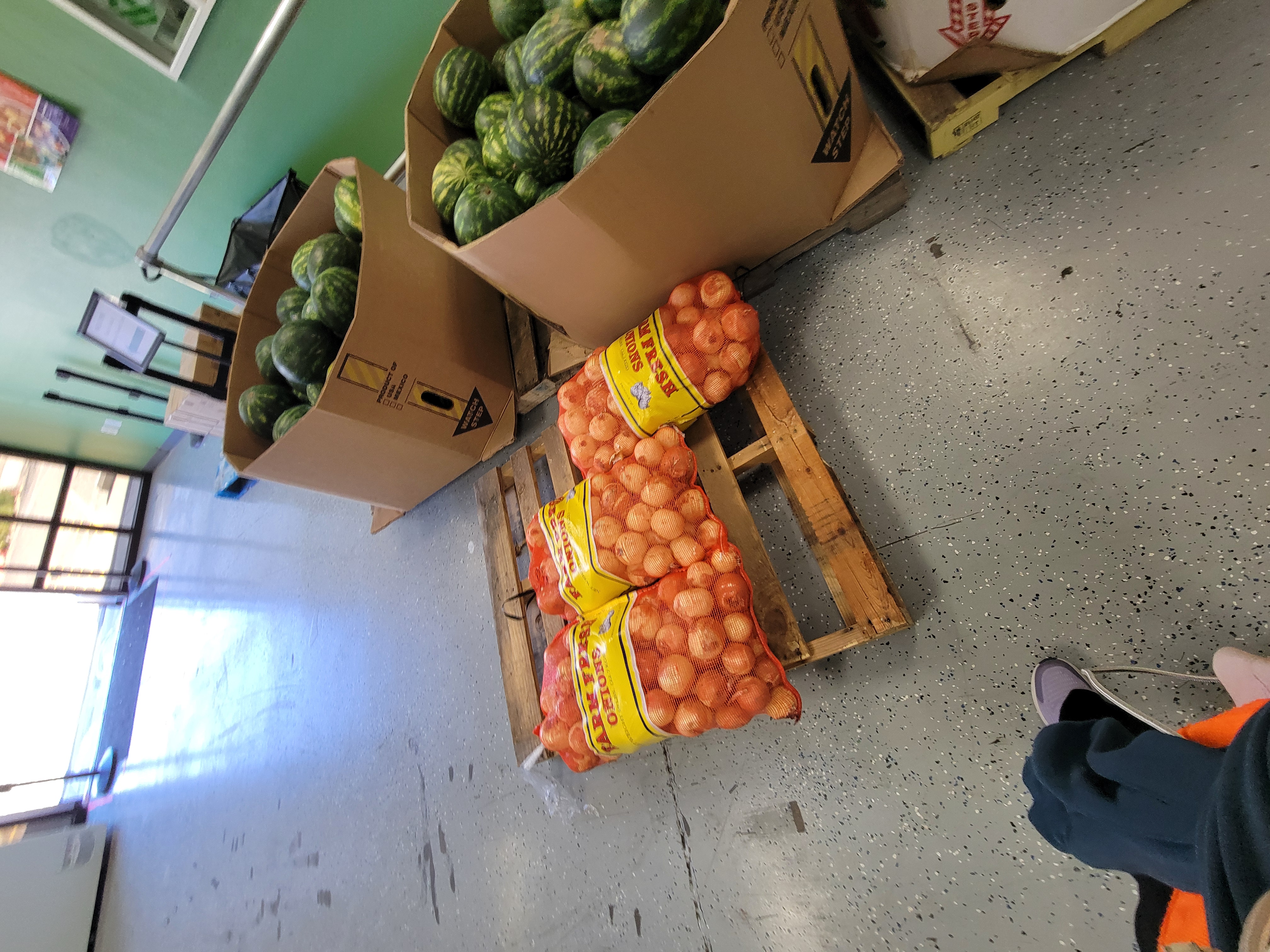 Pallet of bulk bags of onions next to cardboard containers of watermelons.